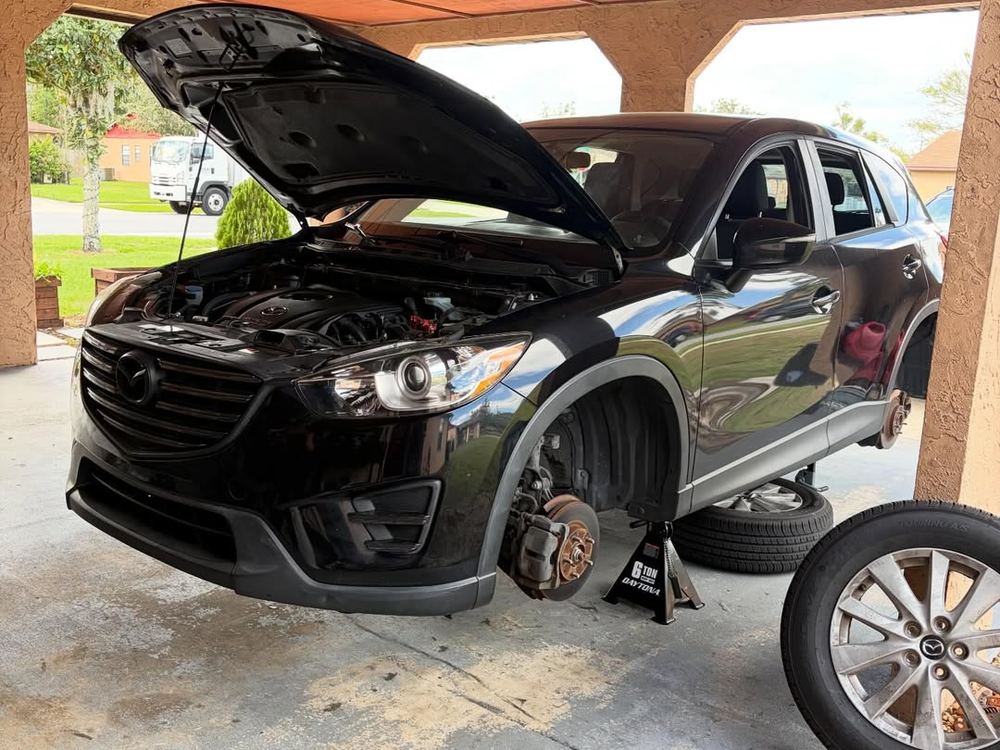 SUV on a jack with the wheel removed for brake work in a carport