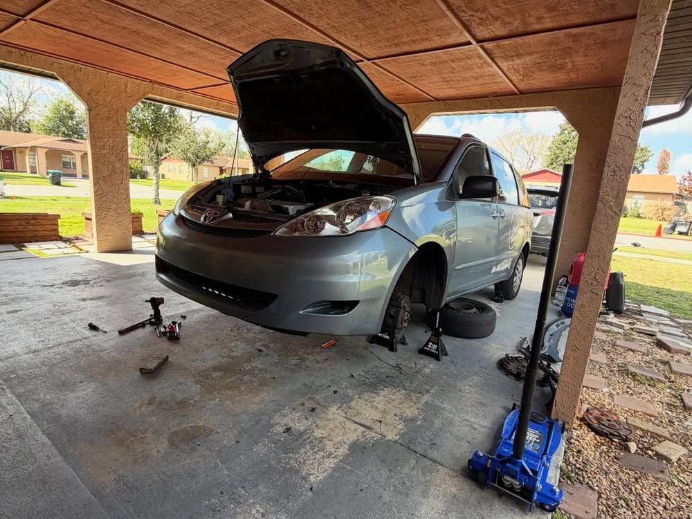 Minivan on stands under a carport with the hood open