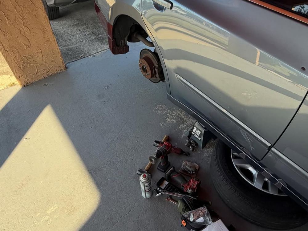 Car on a jack with the wheel off and tools laid out on the ground